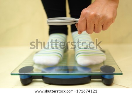 woman feet on weighing scales looking weight over magnifying glass. exaggerate with weight loss concept