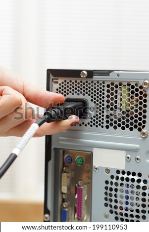 woman inserts power cord into a computer