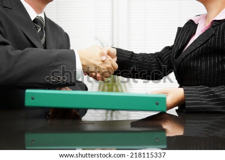 businessman is passing binder with documentation  to his client while handshaking