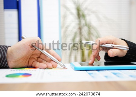 Business colleagues working together on project with tablet computer and paper report