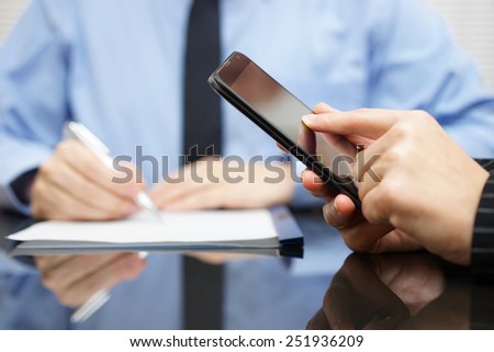 businesswoman is using mobile smart phone and businessman in background is writing on document