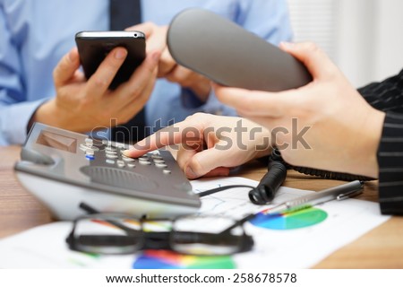 Occupied business people in office are dialing on land line telephone and and using mobile smart phone