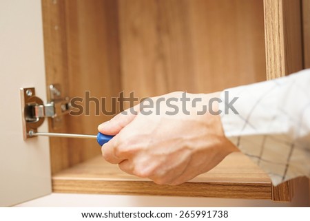 carpenter installing  furniture door hinge and using screwdriver.