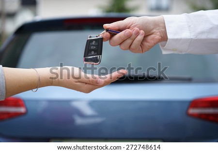 car dealer gives the customer the car keys with car in background