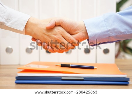 business man and woman are handshaking over documents in with office in background