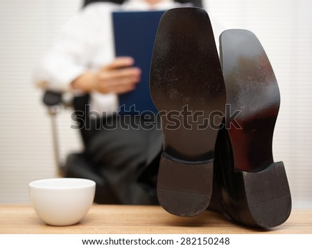 businessman sitting on chair reading report with his feet on the table, focus on shoes