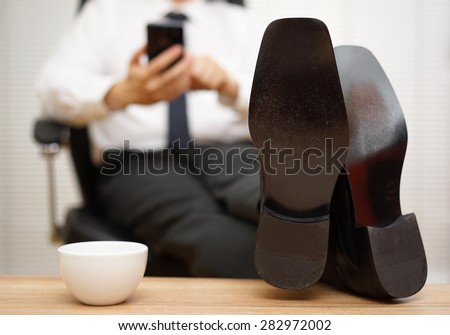 blurred businessman  is working on smart mobile phone, focus on shoes