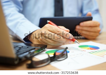 busy businessman overwhelmed with information  on tablet computer, laptop and documentation