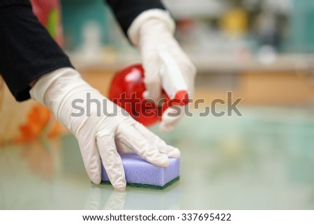 Housemaid from cleaning service is cleaning kitchen with sponge and spray