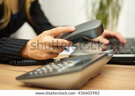 Businesswoman working on laptop computer and picking up telephone handset
