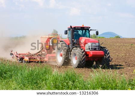 Large red tractor working in the field. Blue sky, brown soil