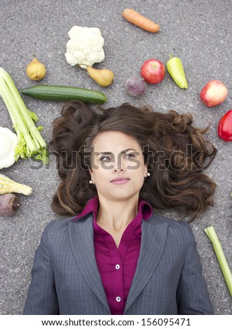 young corporate woman surrounded by vegetables on grey background