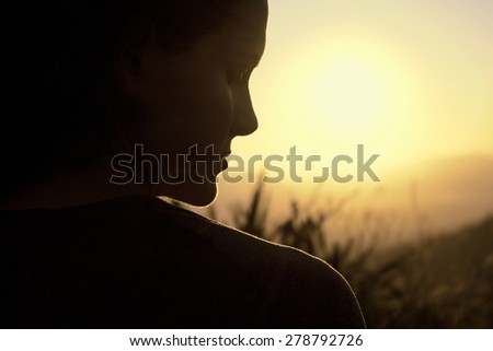Young woman silhouette at sunrise, profile face and landscape background