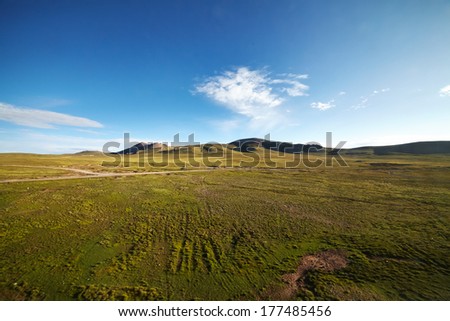 A green plains with mountain landscape in the background against a blue sky at Tibetan Plateau