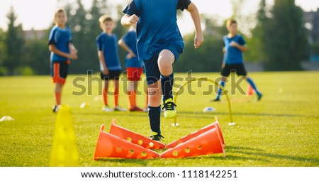 Kid Young Athletes Training with Football Equipment. Football Speed Training. Young Footballer in Blue Sportswear at Training Session on Grass Soccer Field