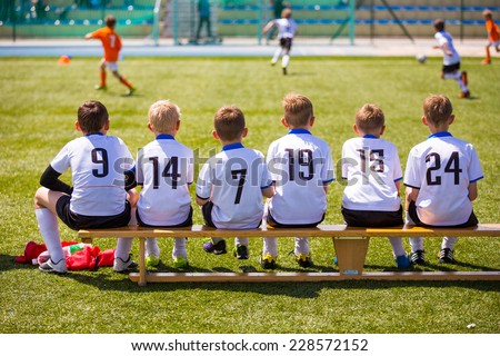 Football soccer match for children. Kids waiting on a bench.