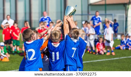 Young Soccer Players Holding Trophy. Boys Celebrating Soccer Football Championship. Winning team of sport tournament for kids children. Horizontal sport background.
