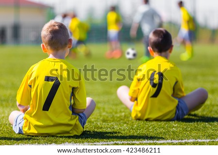 Young football team wearing sports yellow soccer dress. Soccer players on sports field. Football soccer match for children. Youth sports team sitting together and watching football soccer game.