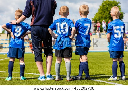 Football soccer match game for children. Youth sports team with soccer coach during football match at the stadium. Kids reserve players waiting on a bench with coach and watching soccer match.