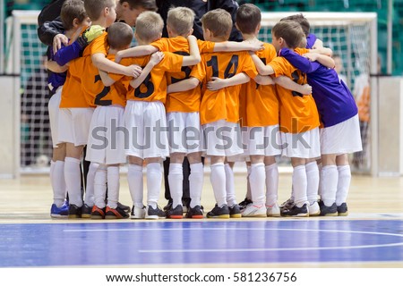 Indoor football soccer match for children. Coach giving young soccer futsal team advices. Youth soccer team before final game. Football match for children. Coach briefing. Soccer football background.