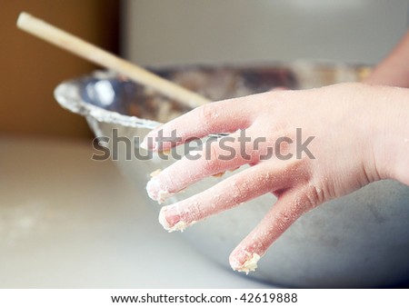 Child\'s soft hand caked with bread dough and flour while mixing and kneading