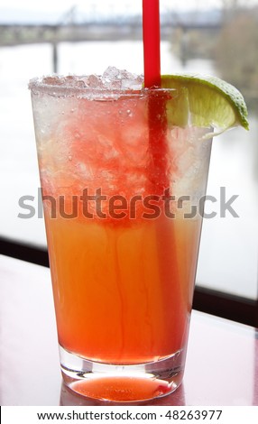 Cold, refreshing, icy margarita with fresh lime wedge and a blush of red color from pomegranate juice
