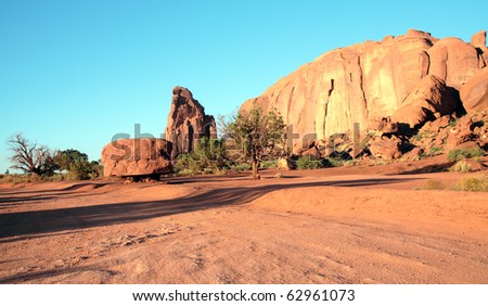 Sandstone rock formations and green trees in Monument Valley desert as sun is setting, casting a golden glow on the landscape