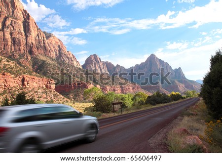 Car drives at high speed along highway through scenic Zion National Park with colorful sandstone and shale mountains and rock formations