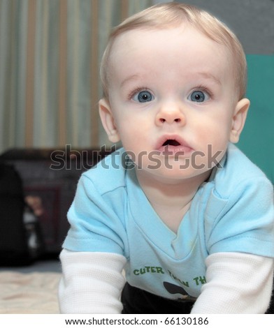 Blonde haired, blue eyed, caucasian baby boy with cute facial expression and look of surprise as he looks into eyes of viewer