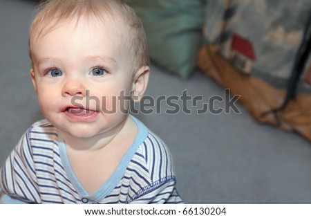 Blonde haired, blue eyed, caucasian baby boy with cute, happy smile making eye contact with viewer