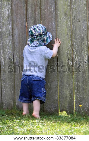 Curious boy peeks through hole in fence to see what is on other side