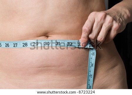 A woman measures her waist with a tape measure. Checking to see if she has reached her weight loss goal. Isolated on a gray background.