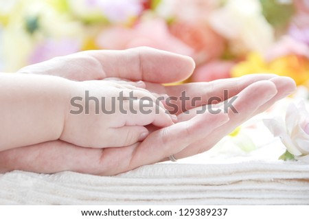 Baby hand on his mother\'s hand in front of beattiful flowers