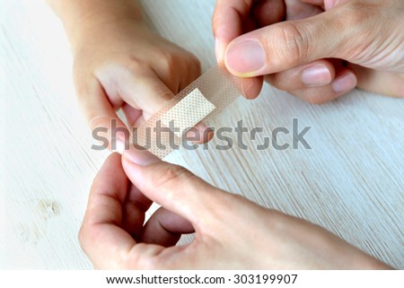 Mother\'s hands putting a plaster on child finger
