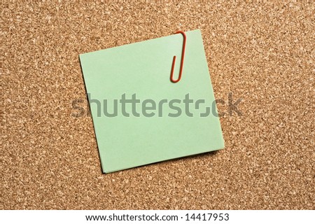 Green paper note with clip on cork board.
