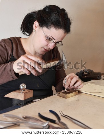 Close-up image of a female jeweler hammering a piece of metal in her workshop. There is an intended motion blur on the hammer.