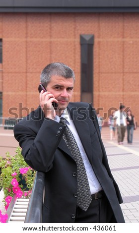 Businessman speaking to the mobile phone-main focus on the hand,the people and the building in the distance are intentionally blurred-the persons are not recognizable.