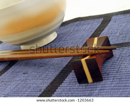Perspective with chopsticks and bowl on a textile blue mat.Soft focus on the pointed end of the chopsticks,main focus in the middle of the image.