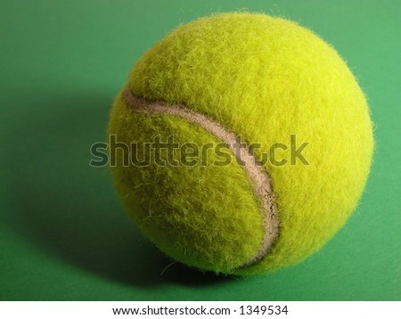 Tennis ball with shadow on a green surface.