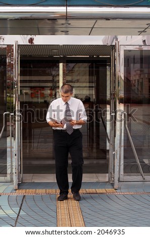A man (businessman or student....) reading with attention a notebook while is walking out from a modern building(corporate or library..... )