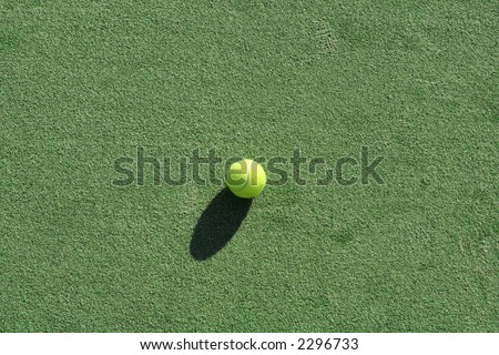 Tennis ball on a green artificial court surface,natural lighting and shadows.
