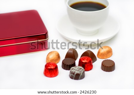Elegant chocolates, a red box and a cup of coffee over white background-festive still life.Selective focus on some chocolates pieces.
