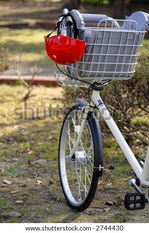 Image of a bicycle handlebar with a kid helmet hanging down in a park.