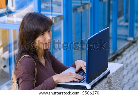 Attractive brunette using a computer somewhere outdoor in the city....in a blue cold tones environment.