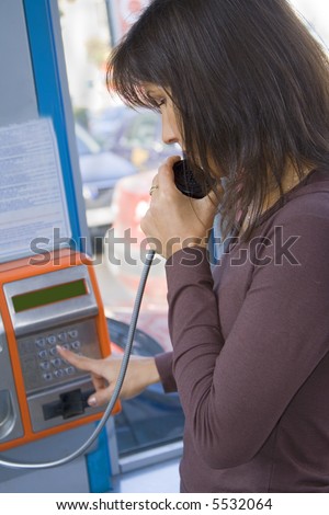 Girl dialing the number in a public phone cabin.Focus on the girl eye and hand.