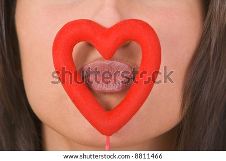 Close-up of woman lips kissing through a red heart shape.