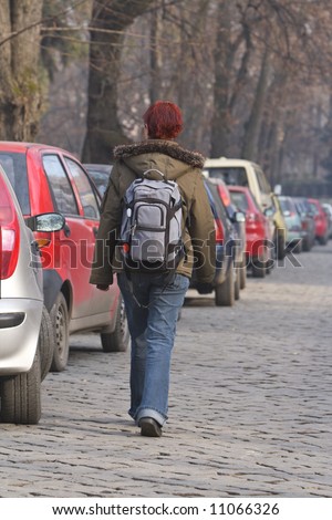 stock photo Redheaded girl with a backpack walking past a row of cars