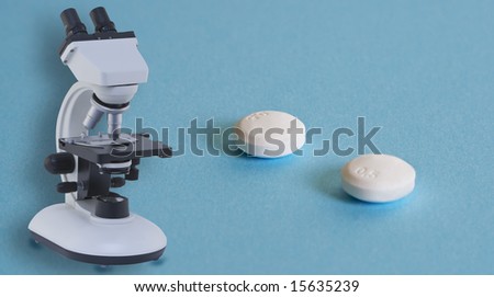 Two aspirin pills and a microscope on a blue surface with some shadows.