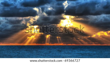 Dramatic sunset rays through a cloudy dark sky over the ocean.