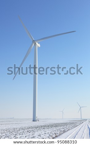 Image of a small road between  wind turbines in a plain covered by snow in winter.